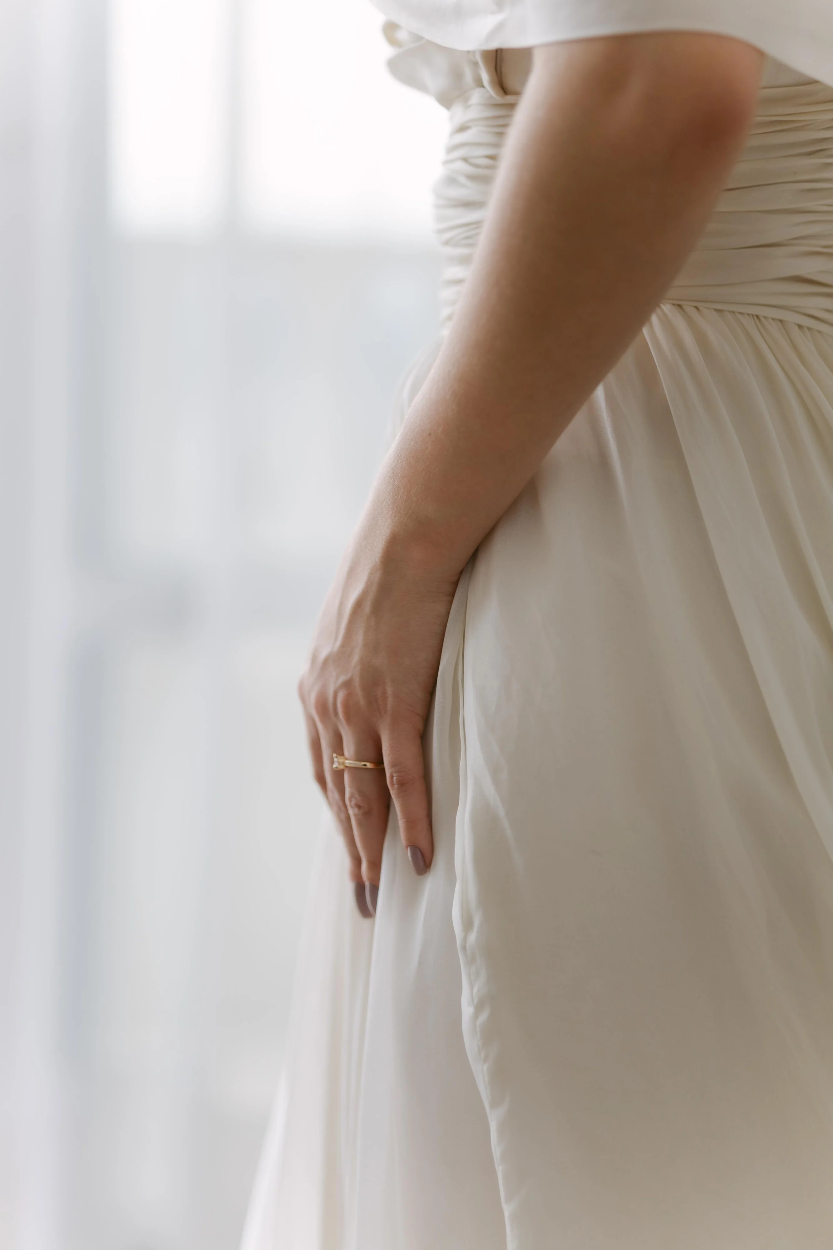 Mão da noiva, de unhas escuras, apoiada no vestido em luz suave