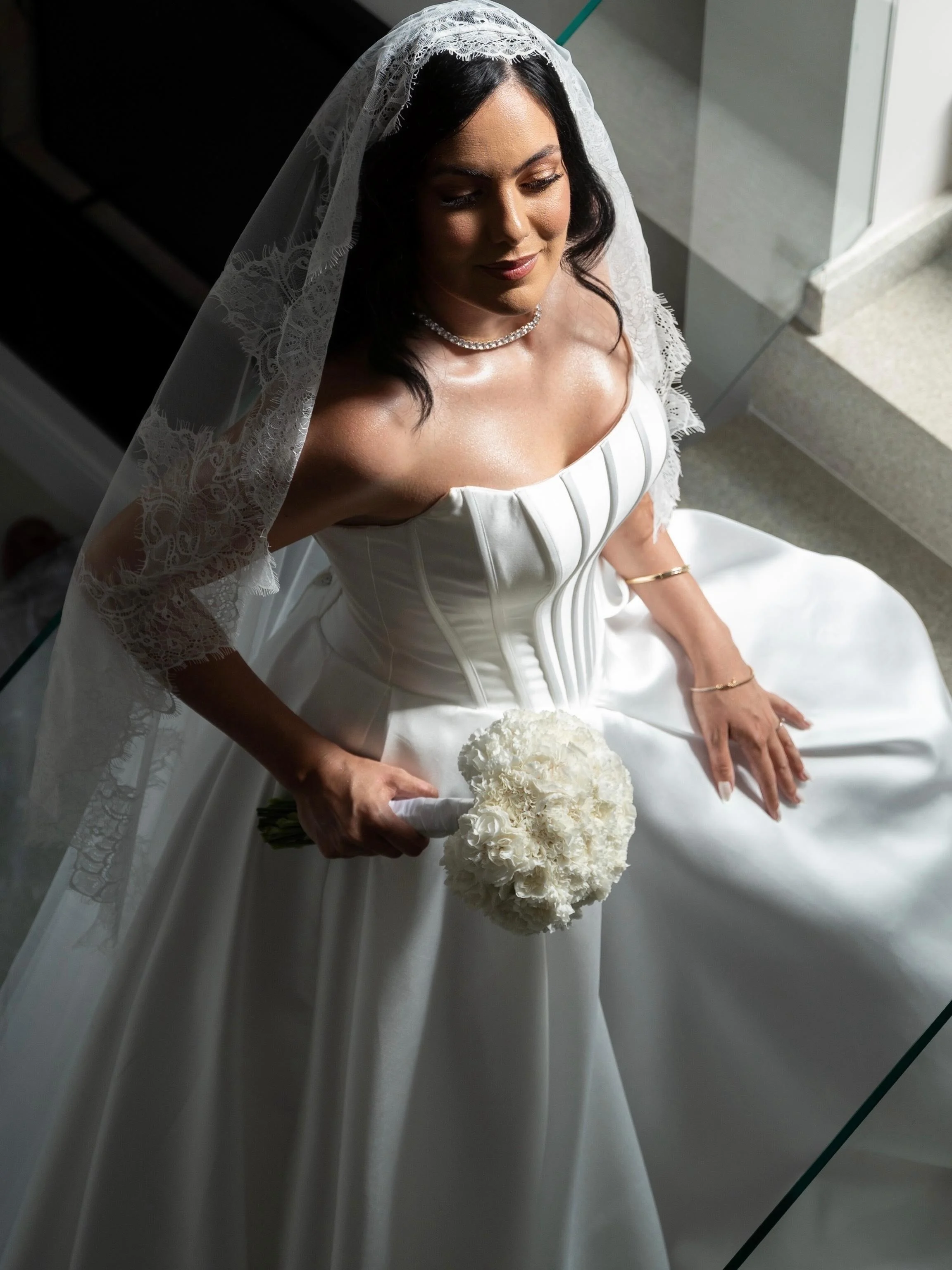 Noiva de véu de renda e buquê branco, pele luminosa e cabelo solto em ondas